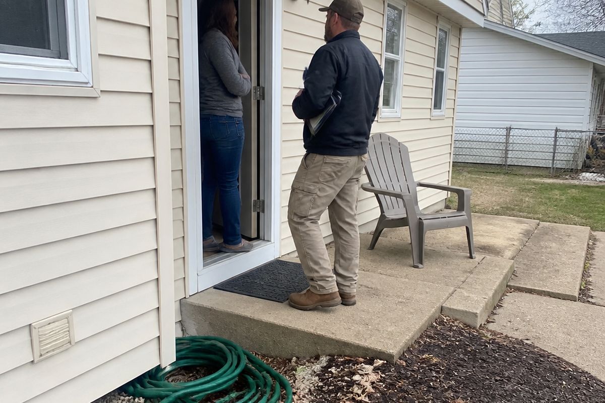 A homeowner and a contractor talking at the open front door of a suburban house.