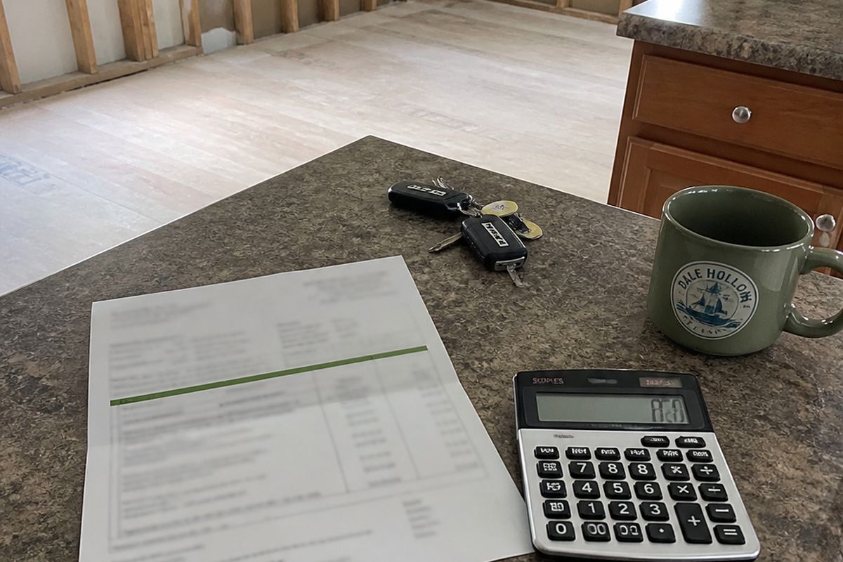 A printed estimate and a calculator on a worn kitchen counter beside truck keys and a mug.